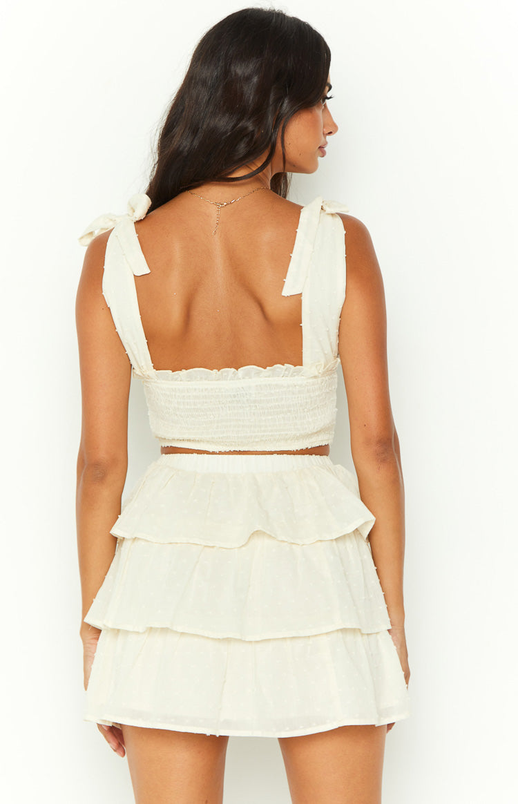 Back view of a cream shoulder tie top with a smocked back panel, ruffled trim, and textured swiss dot fabric