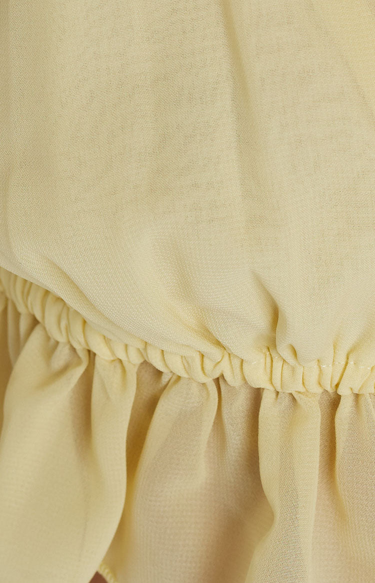 Close-up of the elasticated and gathered hem of a yellow crop top with ruffled detailing