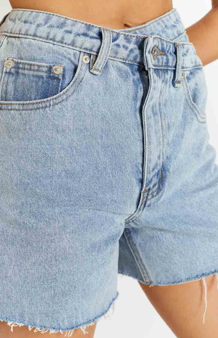 Close-up of the light blue denim shorts showing the front pocket, button fly, and frayed hem