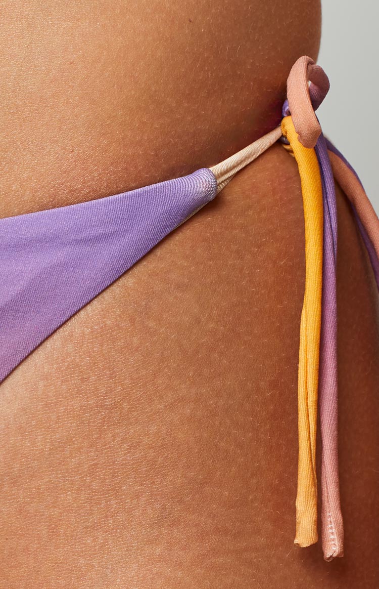Close-up of the side tie detail on the bikini bottoms, featuring lilac fabric and knotted orange, purple, and peach ties