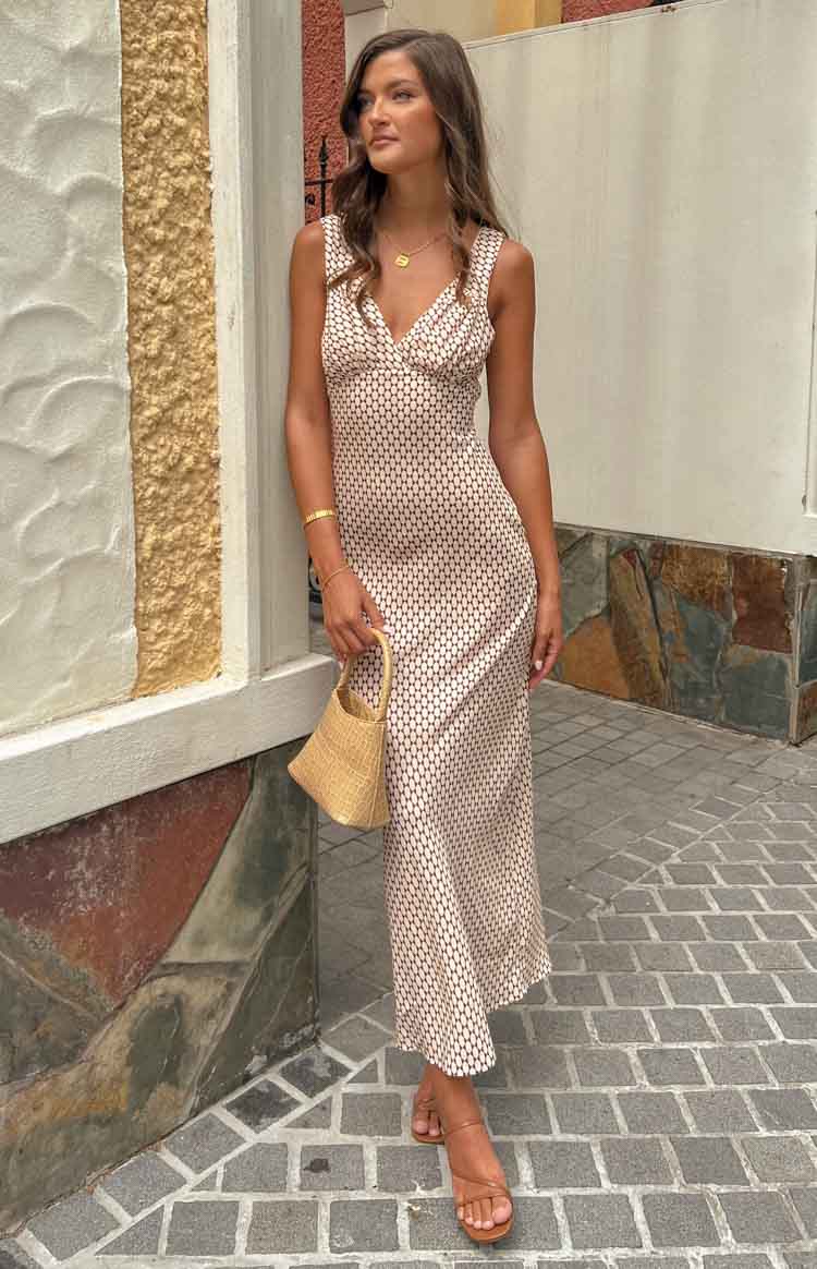 Full length front view of a beige maxi dress with a black geometric pattern, V-neckline, ruched bust, and flowy skirt