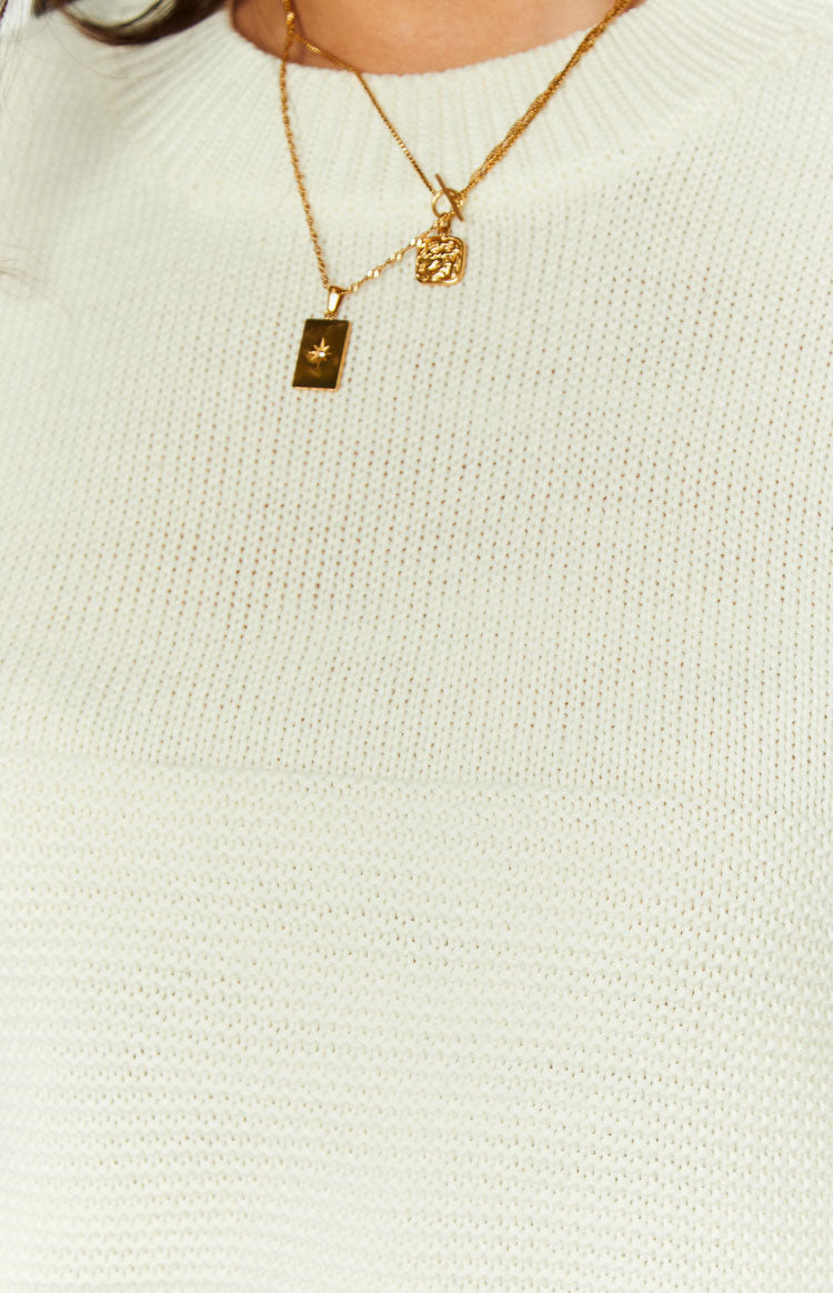 Close-up of the cream knit fabric of a long sleeve top showing the fine texture and crew neckline