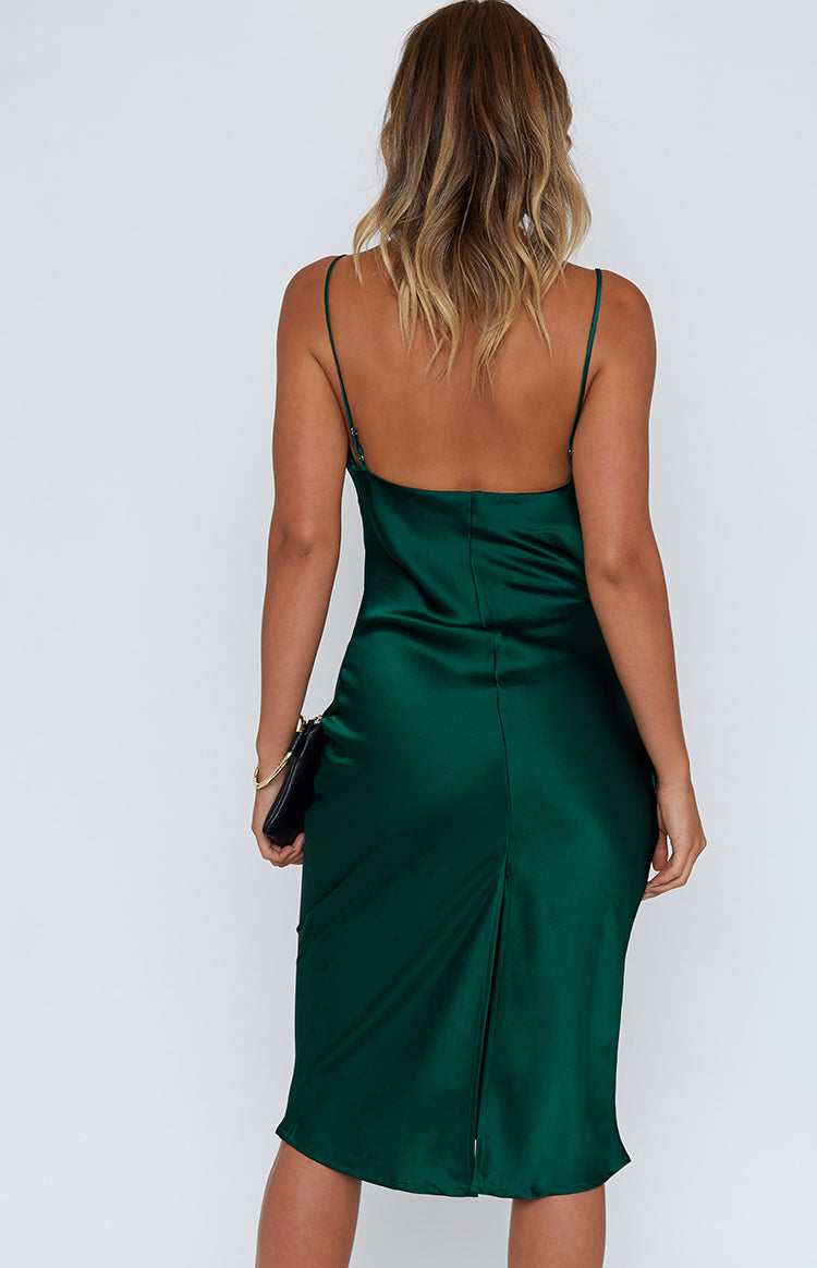 Rear view of an emerald green satin midi dress with thin spaghetti straps, a low scoop back, and a rear hem slit